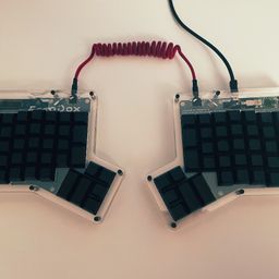 Split ortholinear keyboard with black keycaps on a white table.